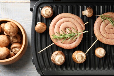 Electric grill with homemade sausages, rosemary and mushrooms on rustic wooden table, flat lay