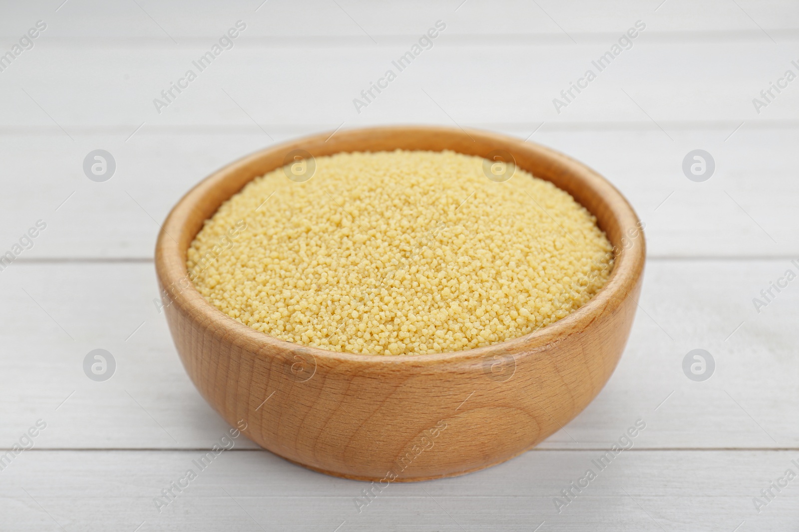 Photo of Bowl of raw couscous on white wooden table, closeup