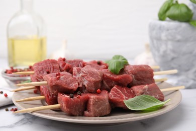 Photo of Wooden skewers with cut fresh beef meat, basil leaves and spices on white table