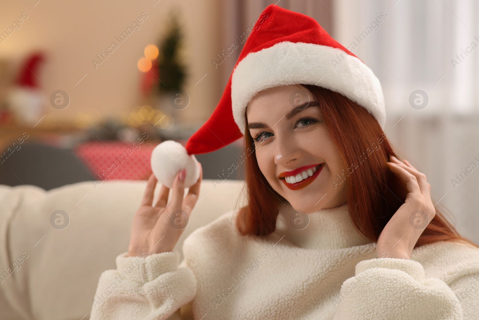 Photo of Beautiful young woman in Santa hat on sofa at home, space for text. Celebrating Christmas