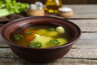 Delicious chicken bouillon with parsley, carrot and eggs on wooden table, closeup