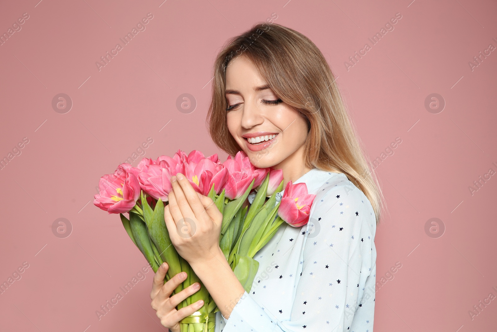 Photo of Portrait of beautiful smiling girl with spring tulips on pink background. International Women's Day