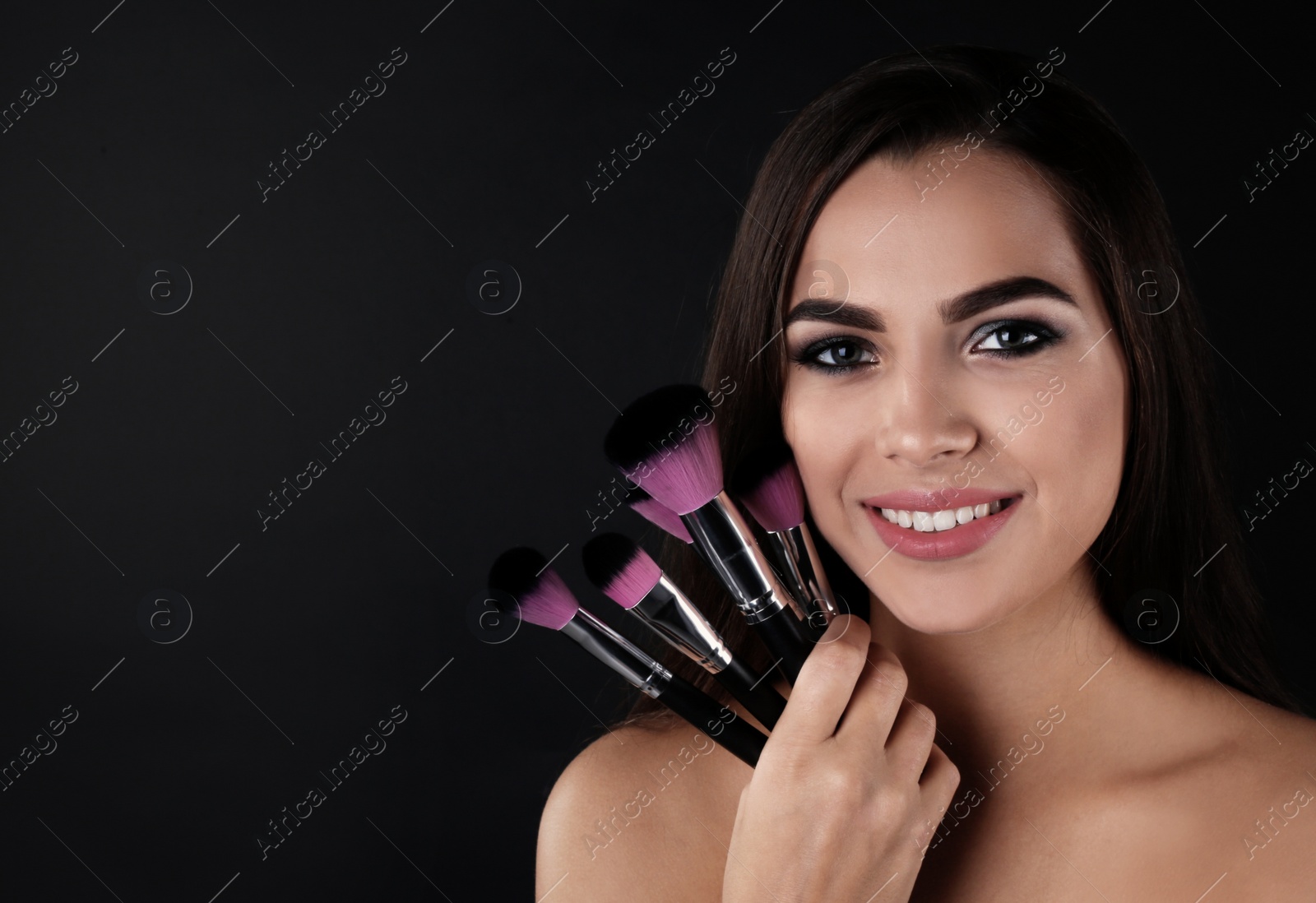 Photo of Portrait of beautiful woman with makeup brushes on dark background. Space for text