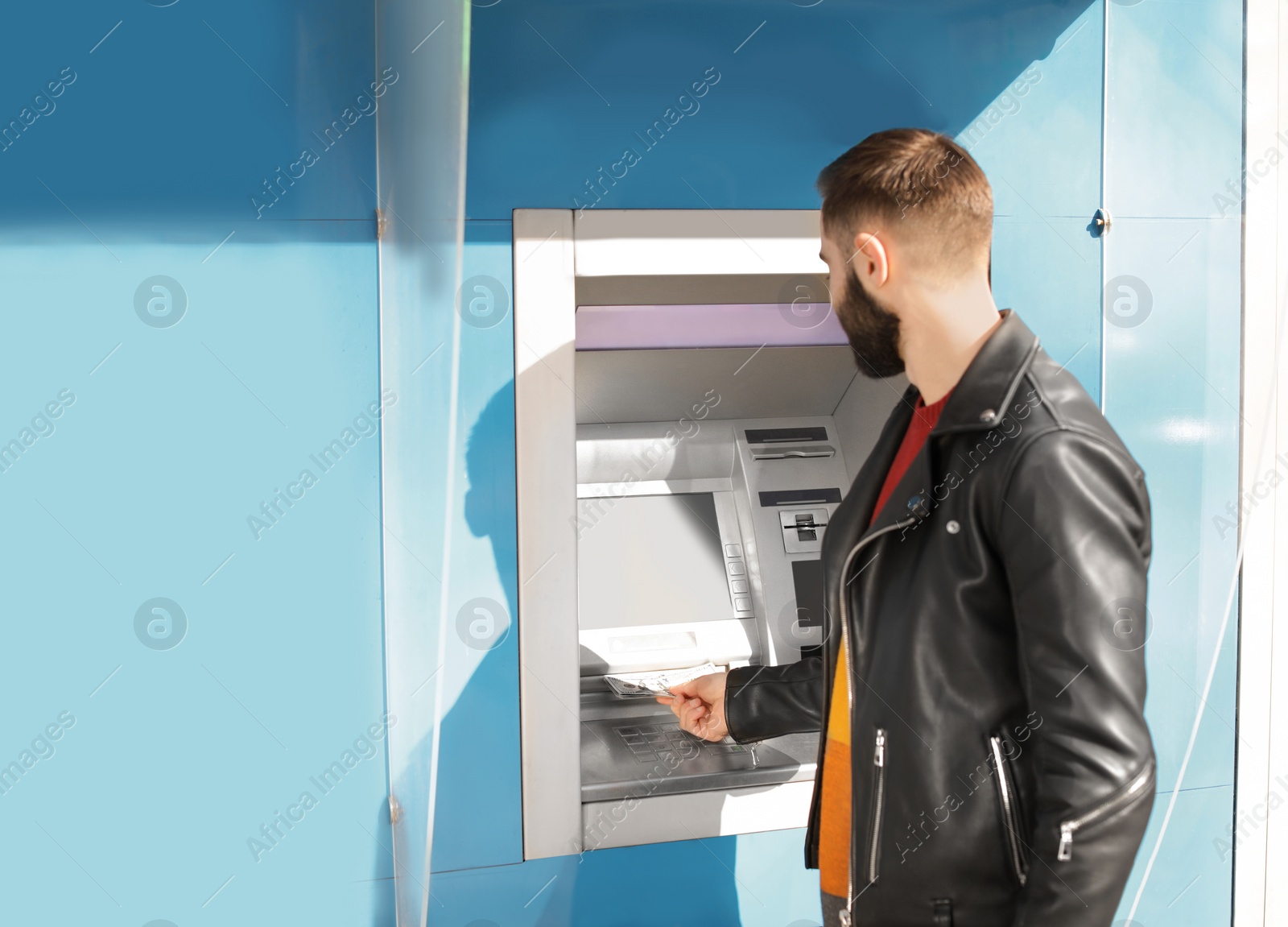 Photo of Young man taking money from cash machine outdoors