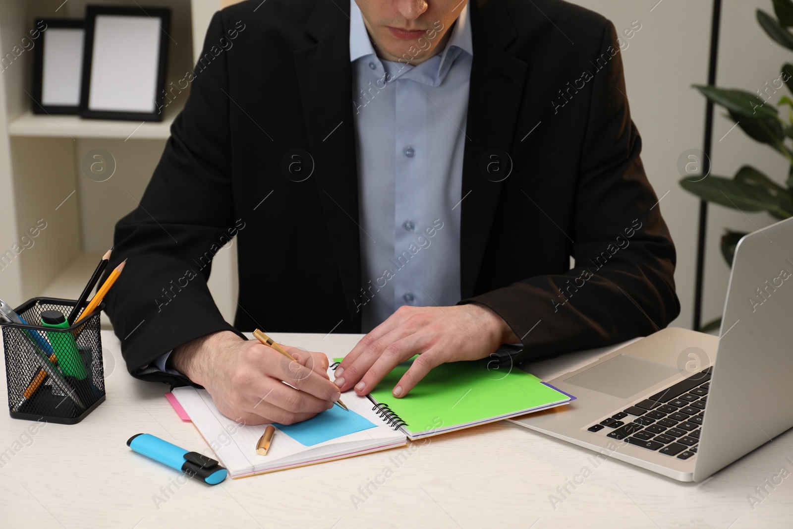 Photo of Man taking notes at white wooden table in office, closeup