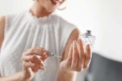 Young woman applying perfume on wrist against blurred background, closeup