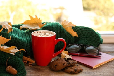 Composition with cup of hot drink, sweater and autumn leaves on windowsill. Cozy atmosphere