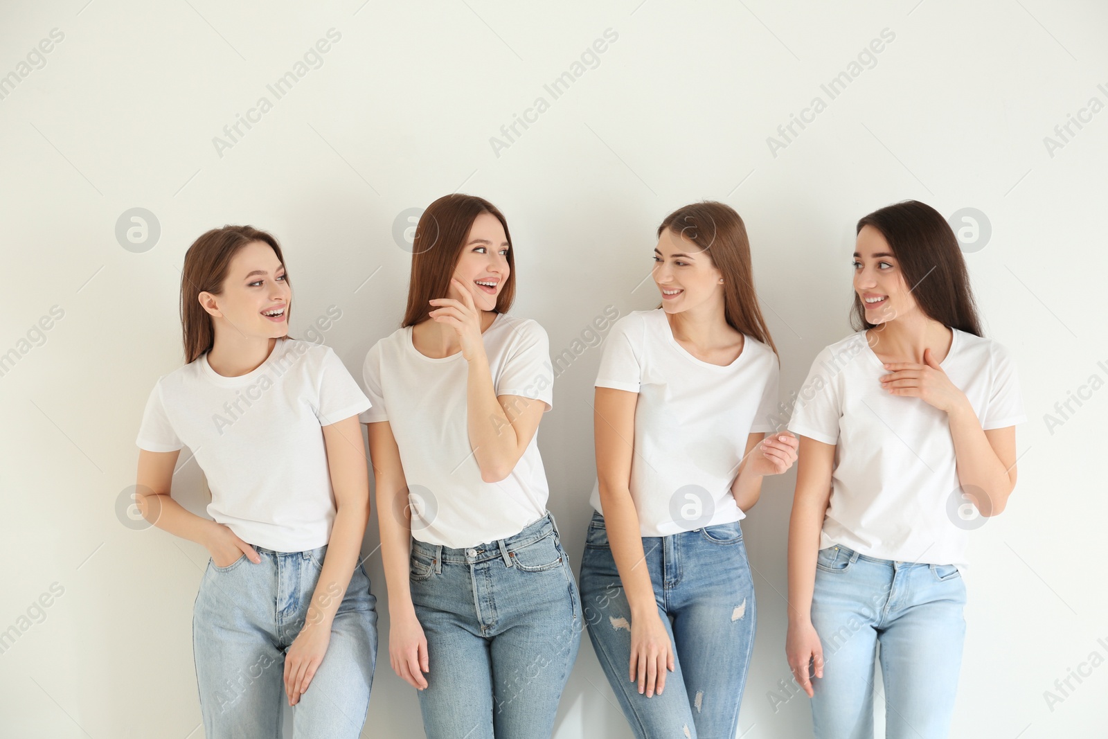 Photo of Beautiful young ladies in jeans and white t-shirts on light background. Woman's Day