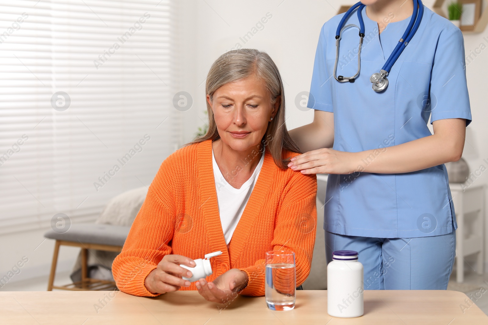 Photo of Senior woman with bottle of pills and young healthcare worker indoors
