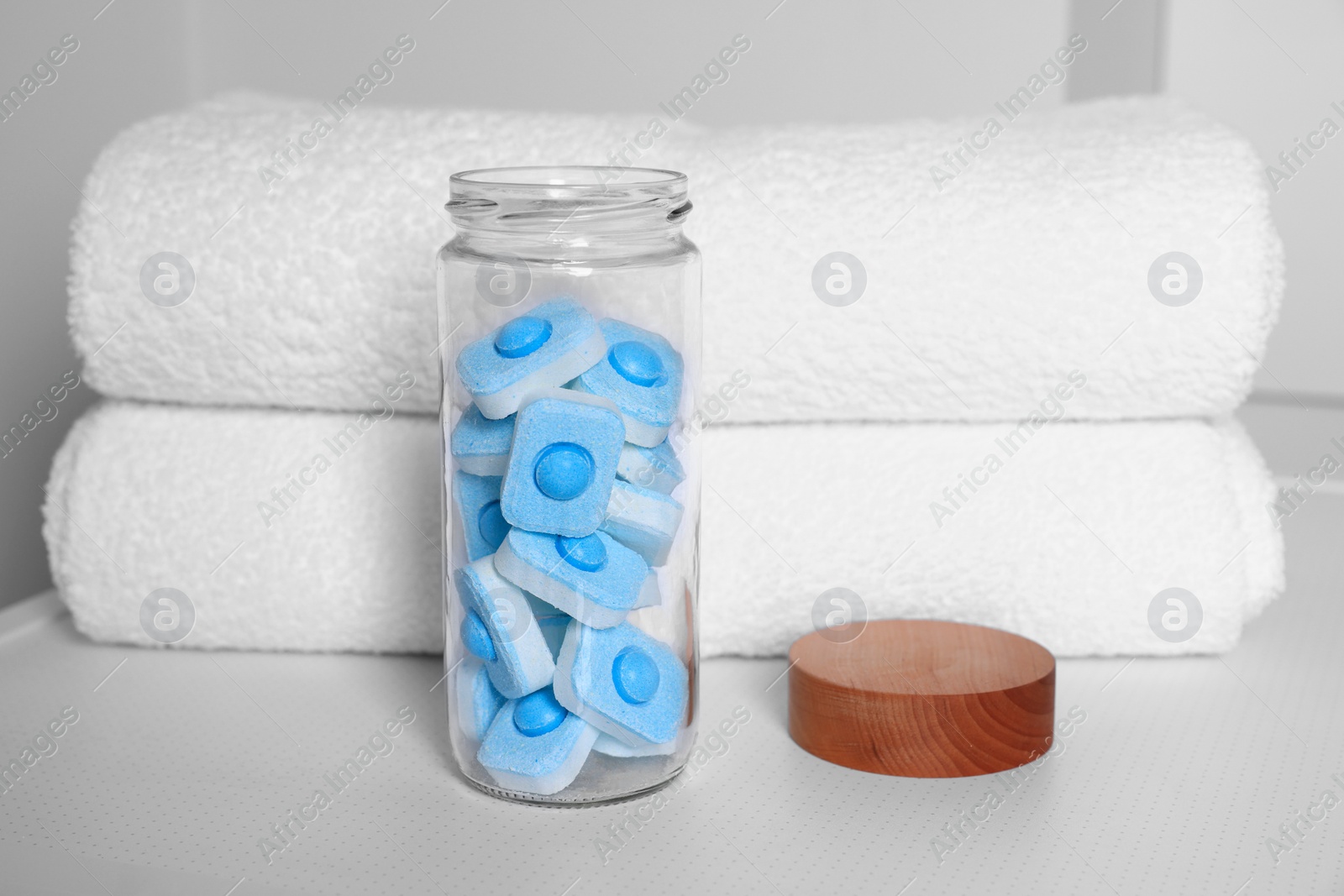 Photo of Glass jar with water softener tablets on washing machine in bathroom