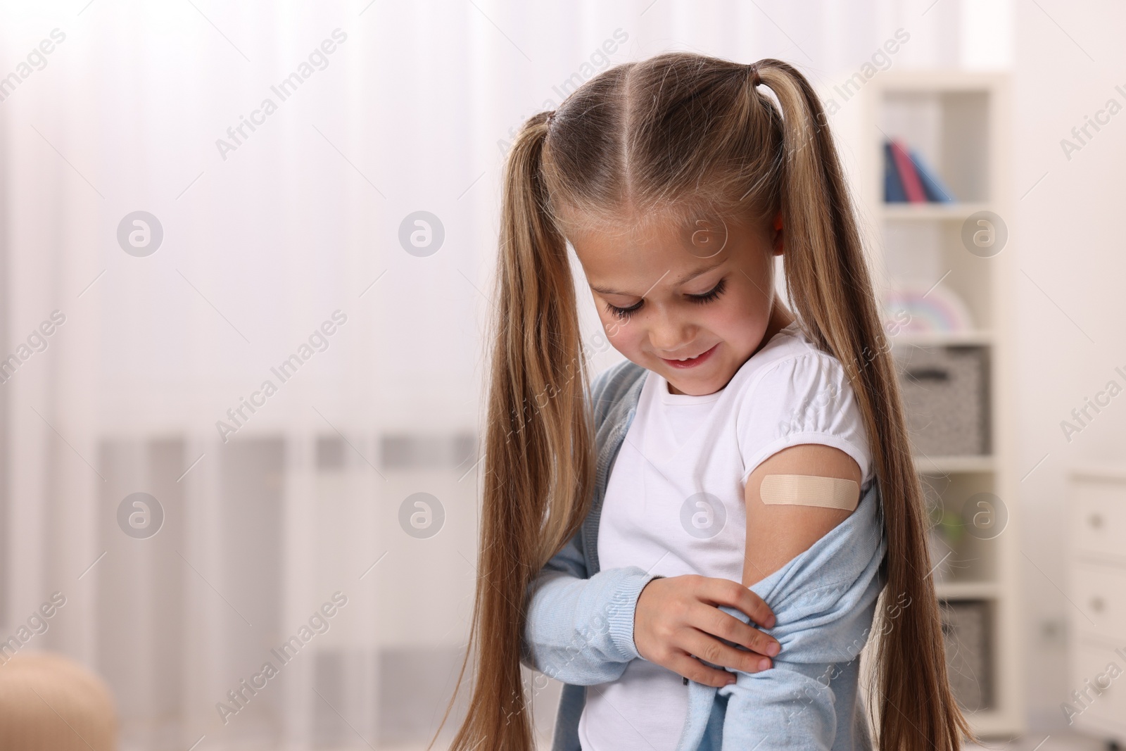 Photo of Girl with sticking plaster on arm after vaccination indoors. Space for text