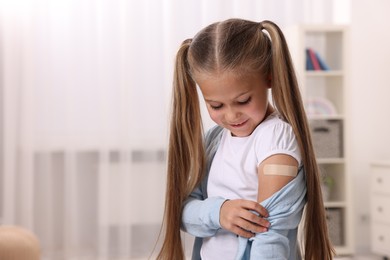 Photo of Girl with sticking plaster on arm after vaccination indoors. Space for text