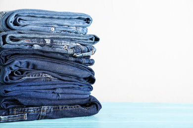 Stack of different jeans on blue wooden table. Space for text