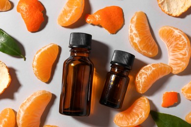 Photo of Aromatic tangerine essential oil in bottles, leaves and citrus fruit on grey table, flat lay