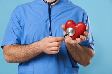Photo of Doctor with stethoscope and red heart on light blue background, closeup. Cardiology concept