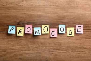 Word Promocode made of colorful paper notes with letters on wooden table, flat lay