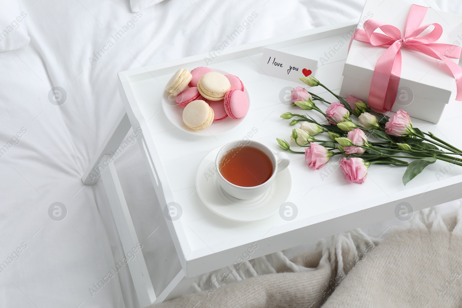 Photo of Tasty breakfast served in bed. Delicious macarons, tea, gift box, flowers and I Love You card on tray