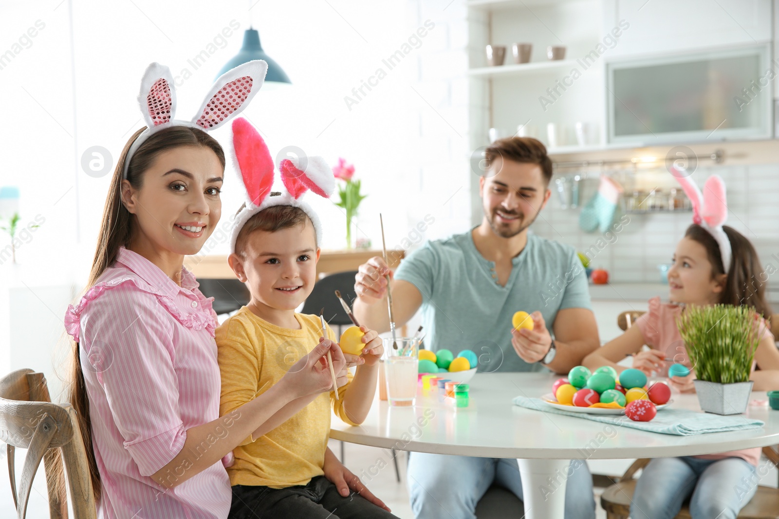 Photo of Happy family painting Easter eggs in kitchen. Festive tradition