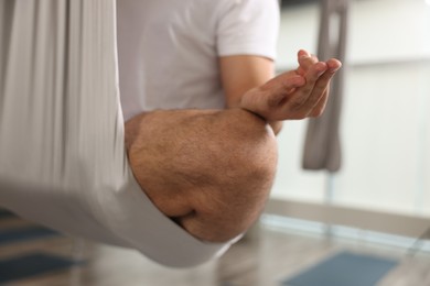 Photo of Man meditating in fly yoga hammock indoors, closeup