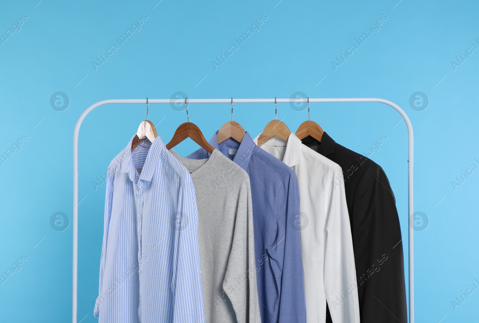 Photo of Rack with stylish clothes on wooden hangers against light blue background