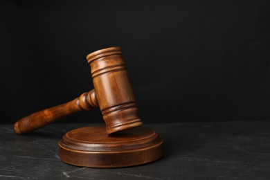 Photo of Wooden gavel on dark textured table, closeup. Space for text