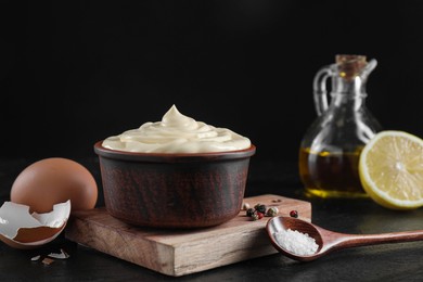 Photo of Fresh mayonnaise sauce in bowl and ingredients on black table, closeup