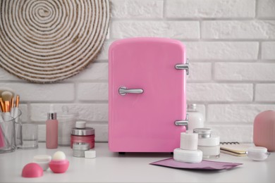 Photo of Mini fridge for cosmetic products on white vanity table