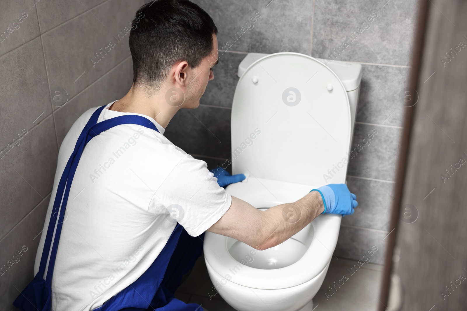 Photo of Plumber wearing protective gloves repairing toilet bowl in water closet