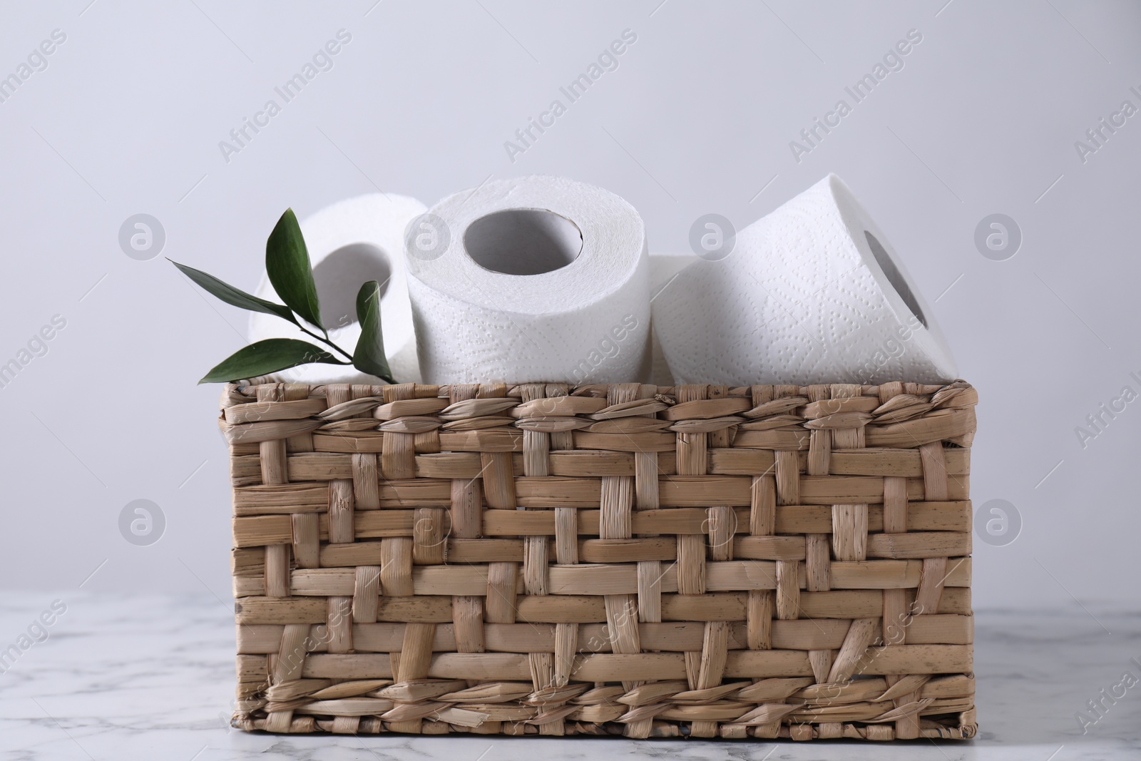 Photo of Toilet paper rolls and green leaves in wicker basket on white marble table