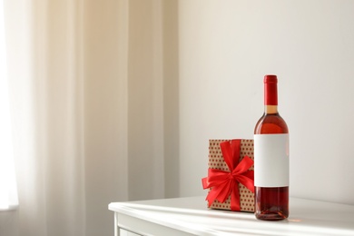 Photo of Bottle of wine and gift box on table in light room. Space for text