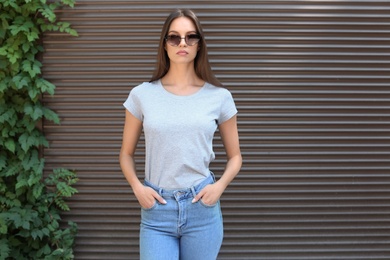 Photo of Young woman wearing gray t-shirt near wall on street. Urban style