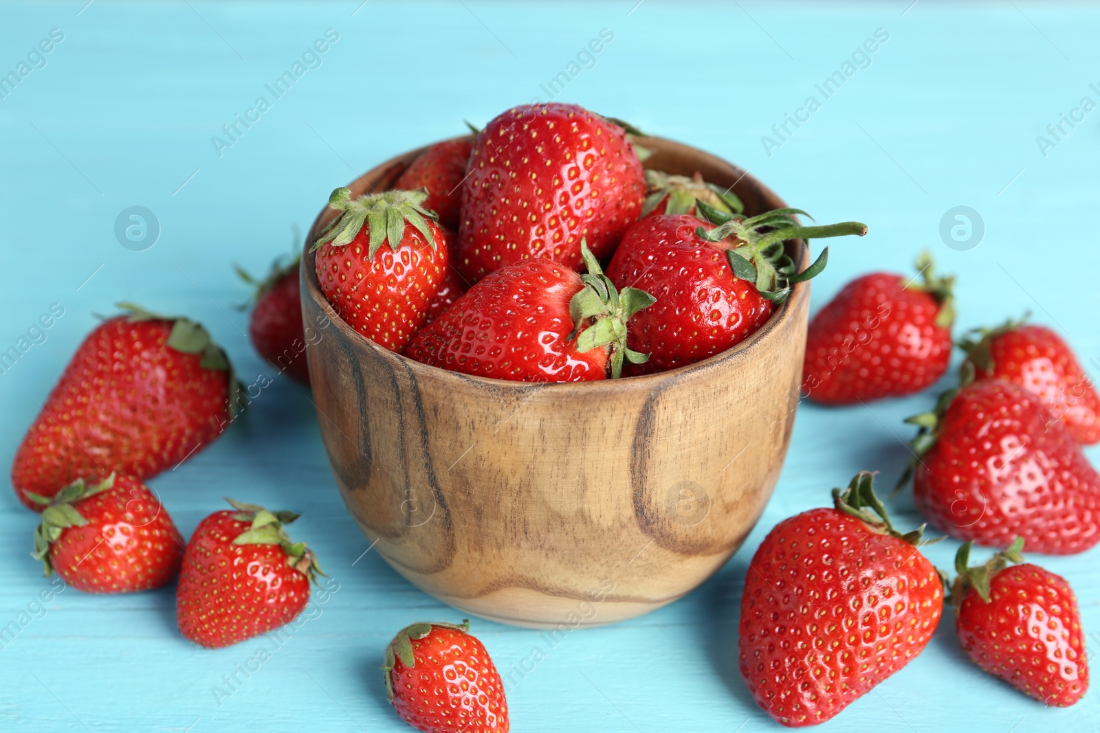 Photo of Delicious ripe strawberries in bowl on light blue wooden table