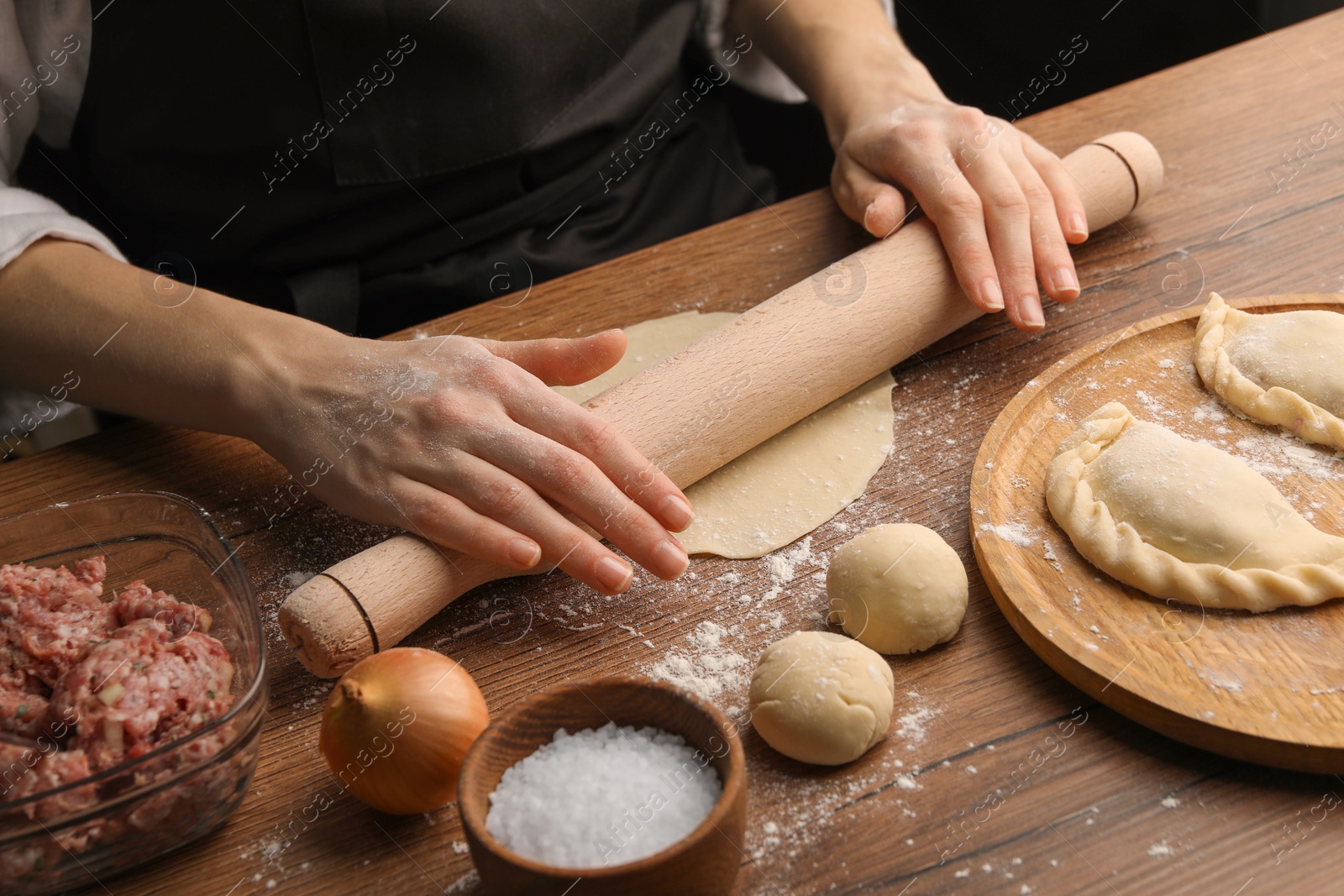 Photo of Woman rolling dough for chebureki on wooden table, closeup