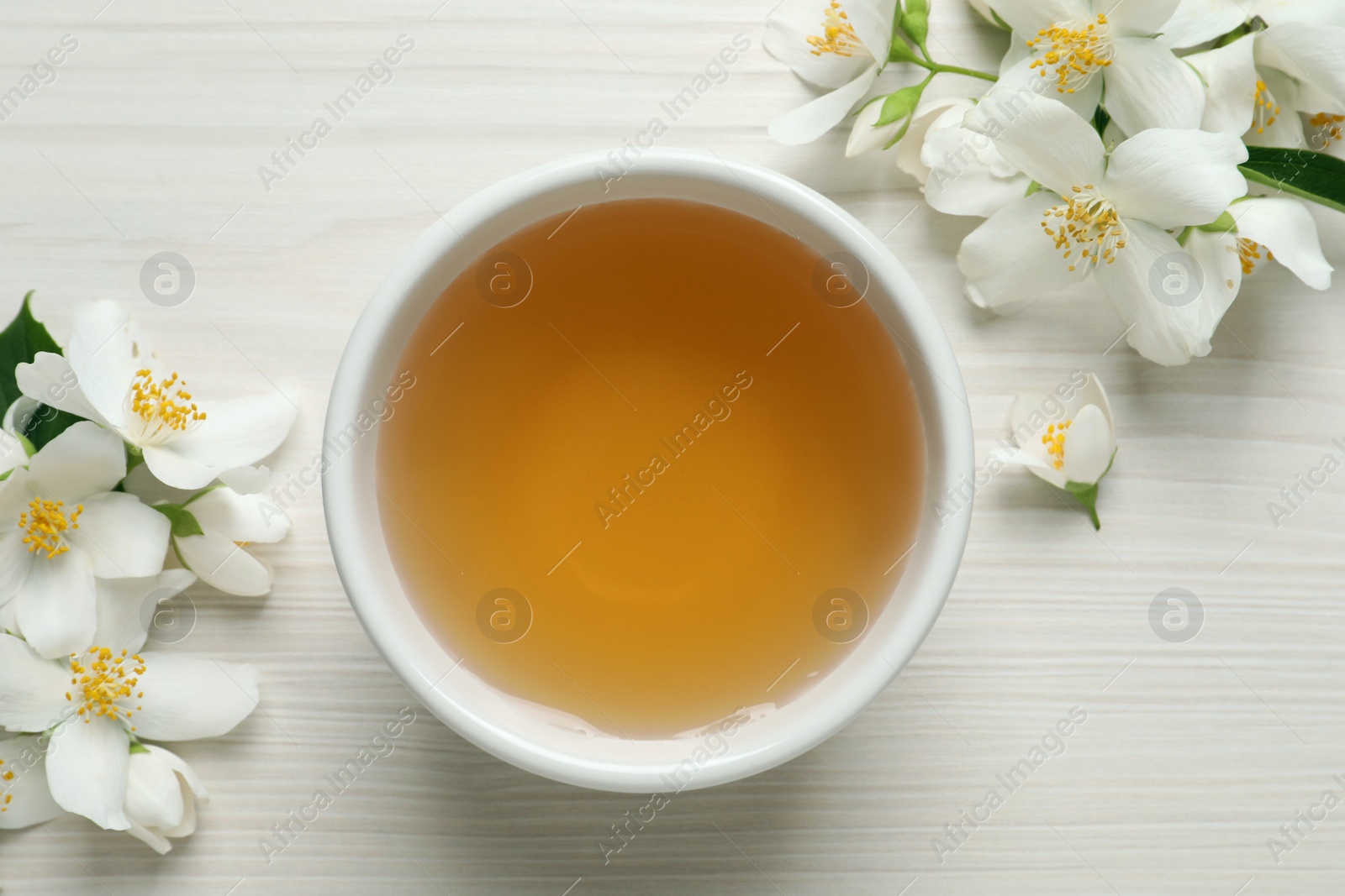 Photo of Aromatic jasmine tea and fresh flowers on white wooden table, flat lay