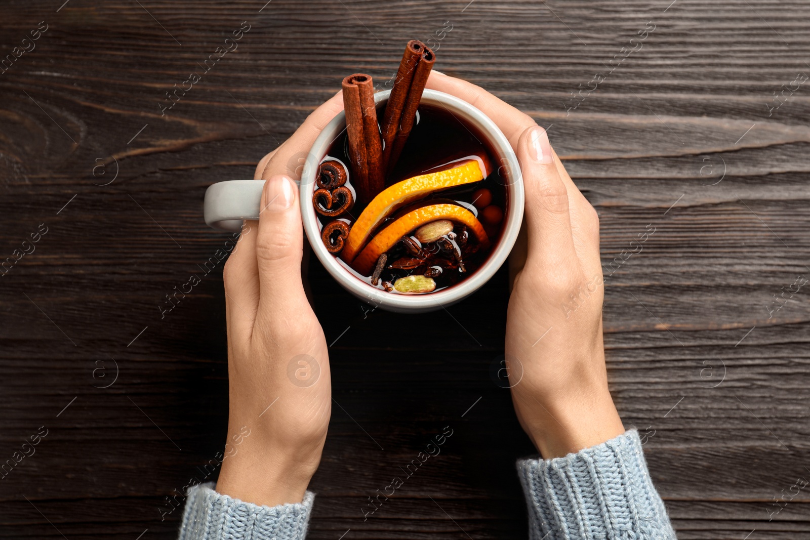 Photo of Woman holding cup of tasty mulled wine at black wooden table, top view