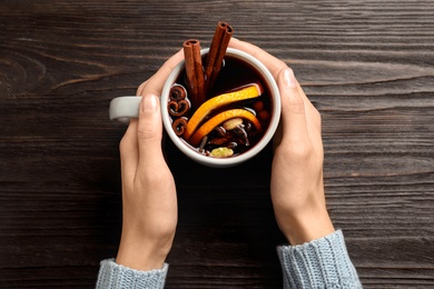 Photo of Woman holding cup of tasty mulled wine at black wooden table, top view