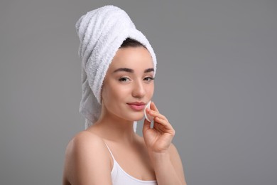 Photo of Beautiful woman in terry towel removing makeup with cotton pad on gray background, space for text