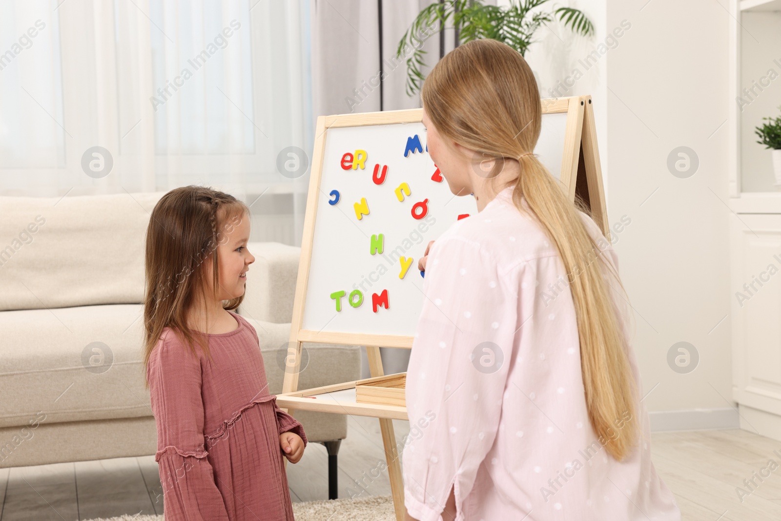 Photo of Mom teaching her daughter alphabet with magnetic letters at home