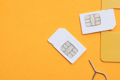 Photo of Modern SIM cards and needle on orange background, flat lay. Space for text