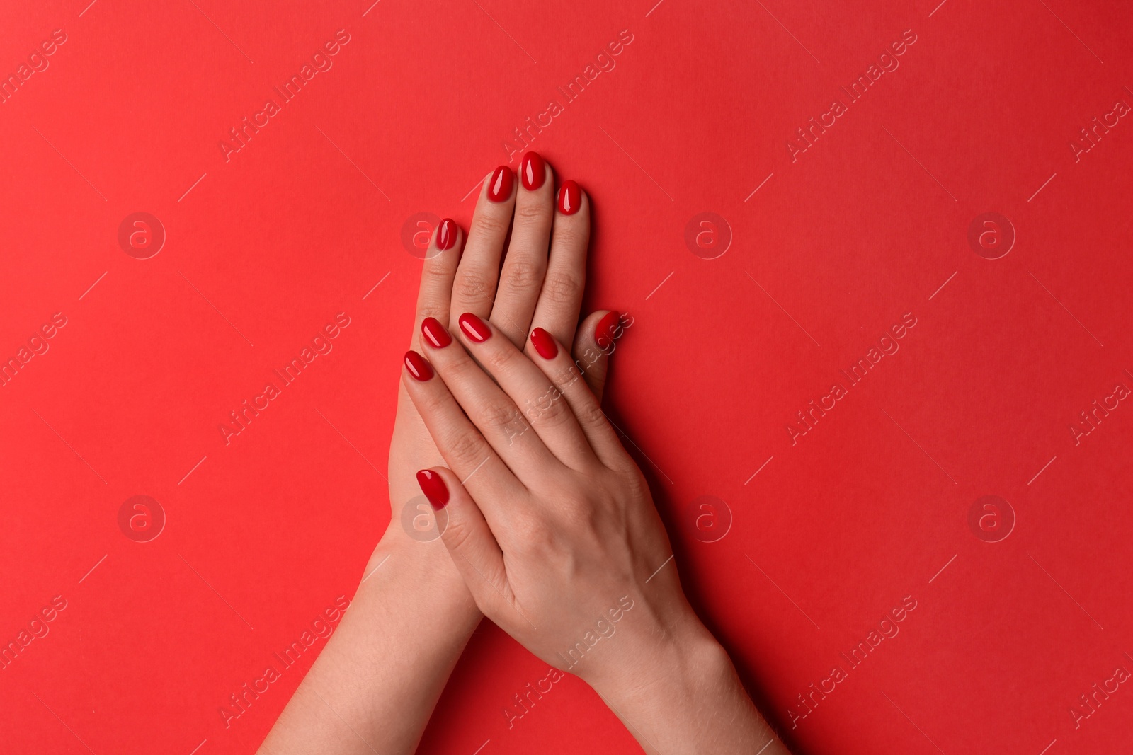 Photo of Woman with gel polish on nails against red background, top view