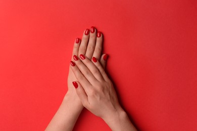 Photo of Woman with gel polish on nails against red background, top view