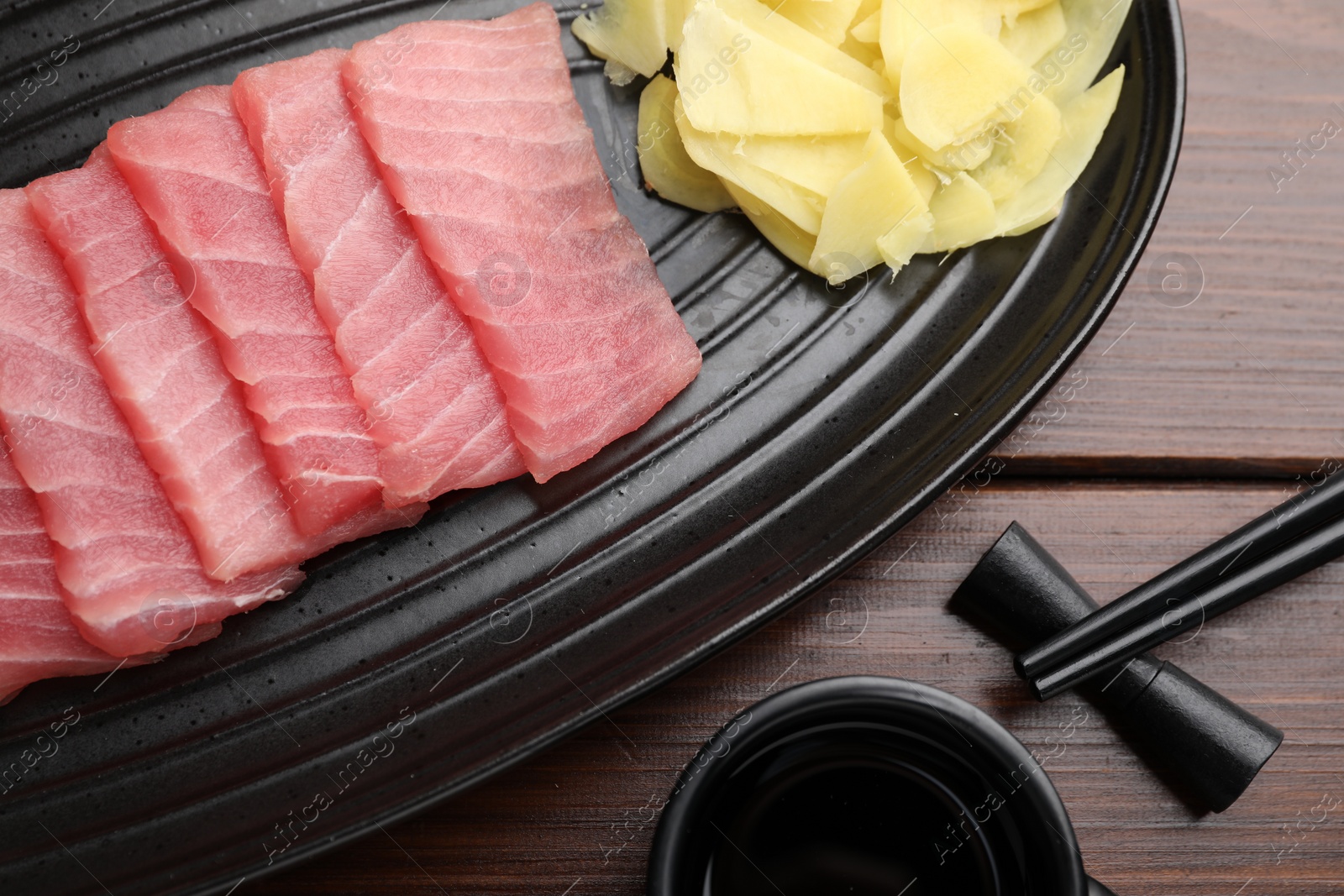 Photo of Tasty sashimi (piece of fresh raw tuna), ginger slices and soy sauce on table, flat lay