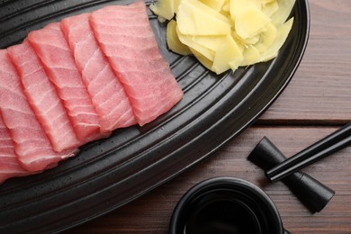 Tasty sashimi (piece of fresh raw tuna), ginger slices and soy sauce on table, flat lay