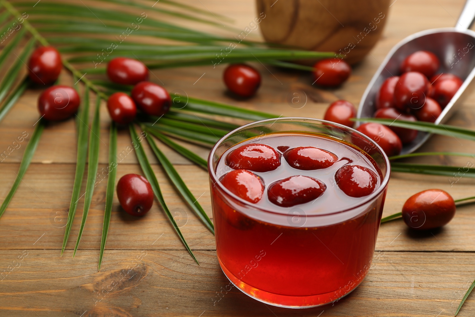 Photo of Palm oil in glass bowl with fruits and tropical leaf on wooden table