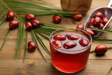 Photo of Palm oil in glass bowl with fruits and tropical leaf on wooden table