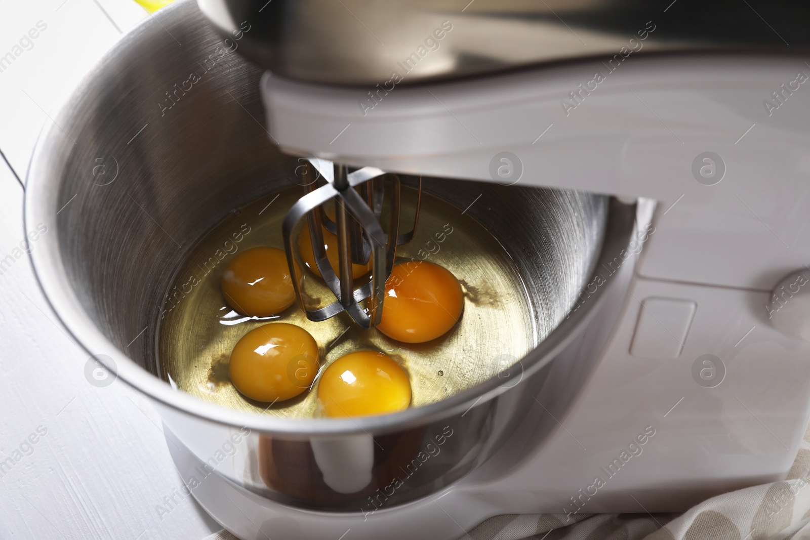 Photo of Making dough. Raw eggs in bowl of stand mixer on white table, closeup