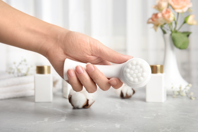Photo of Woman holding face cleansing brush over light grey marble table, closeup. Cosmetic accessory