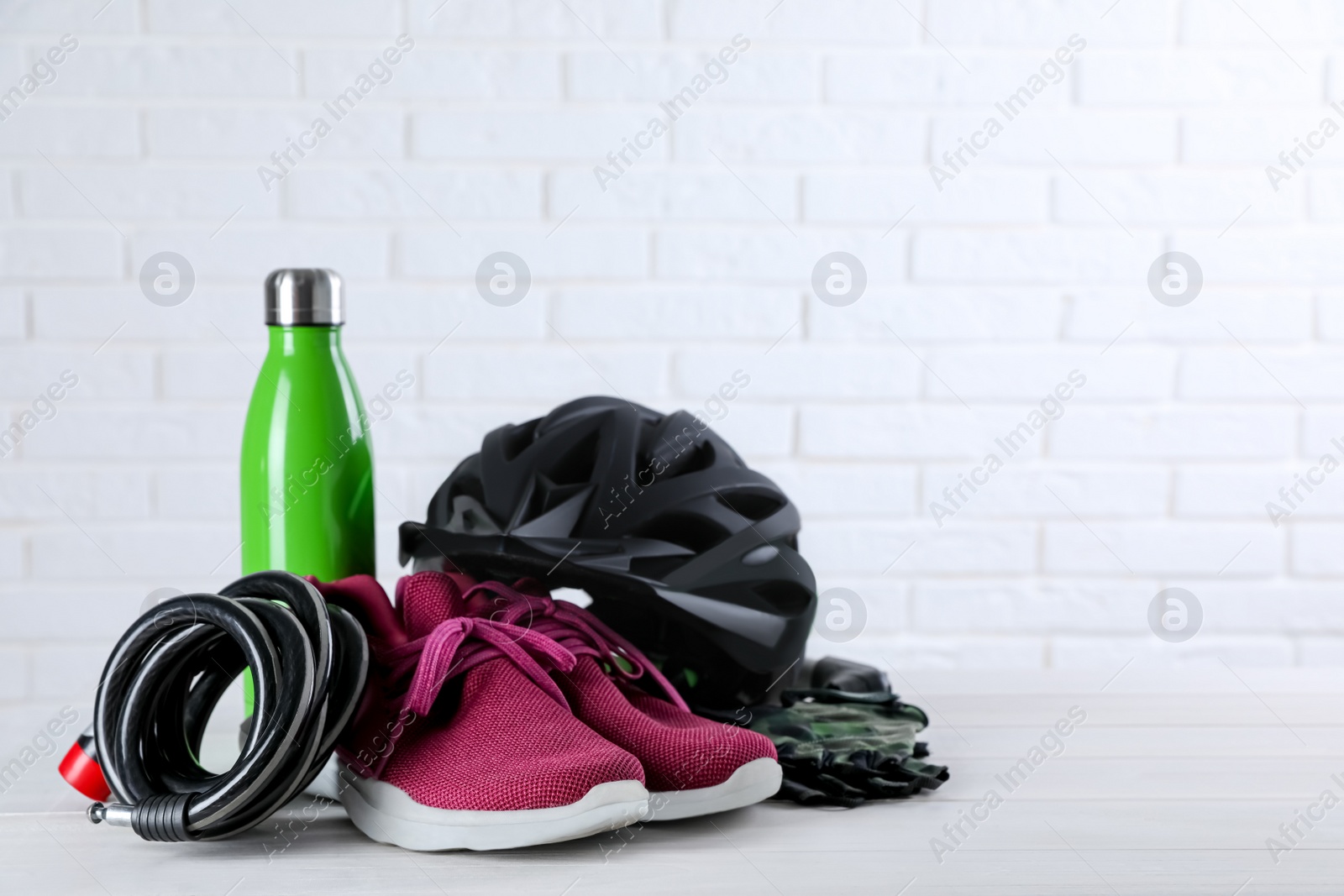 Photo of Different cycling accessories on white wooden table against brick wall, space for text