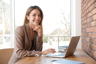 Photo of Young businesswoman using laptop at table in office