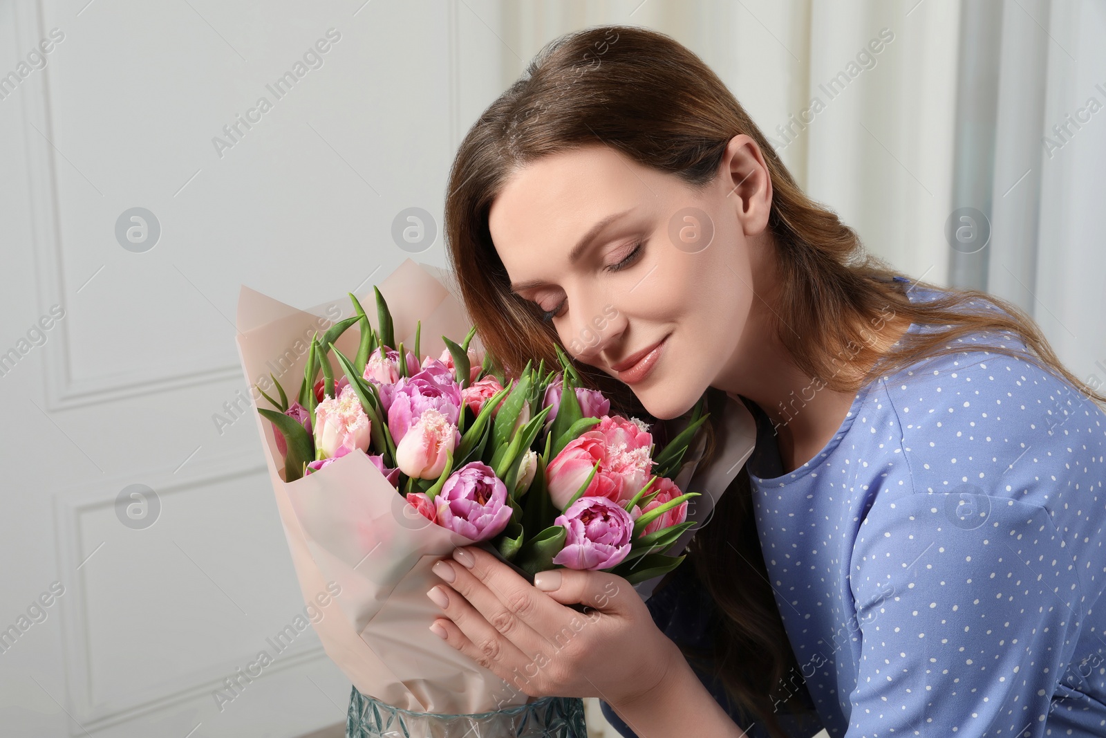 Photo of Young woman with bouquet of beautiful tulips indoors. Space for text